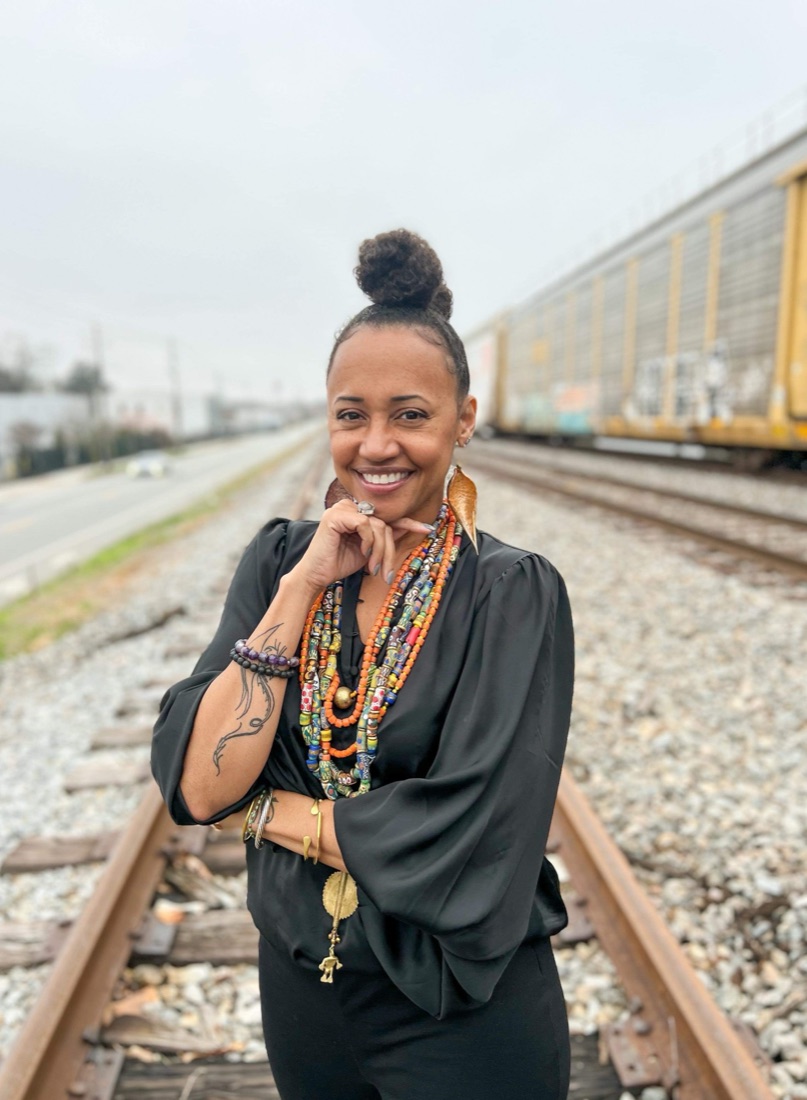 DJ SkyyWalker, smiling, in a black blouse and layered beaded necklaces