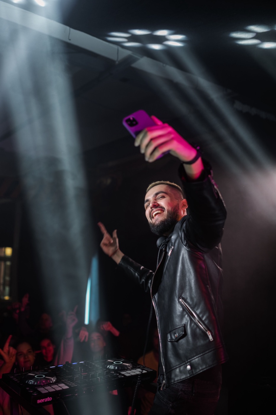 A DJ at their controller, holding up a phone mid-set